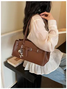 Detailed shot of brown leather shoulder bag with buckle and cute balloon dog keychain accessory.