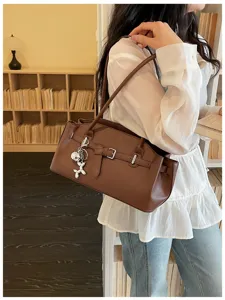 Detailed shot of a stylish brown leather shoulder bag with chic belt buckle and cute charm.