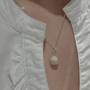 Primo piano dettagliato di una collana con ciondolo cupcake in argento su camicia bianca.