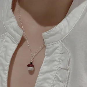 Primo piano dettaglio del ciondolo collana cupcake in argento su camicia bianca stile.