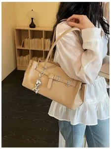 Chic beige shoulder bag for women, stylish underarm handbag with metallic charm and belt design.