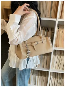 Detailed view of beige shoulder bag with metal buckle and cute charm, commuter style.