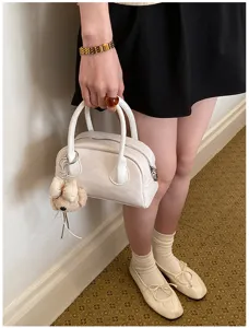 Casual white handbag detail shot featuring dual top handles and cute bear charm pendant.