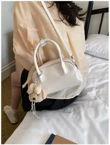 Detailed view of the stylish white shoulder handbag featuring a cute bear charm and strap.