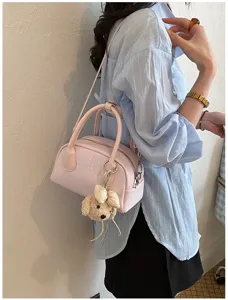 Detail view of a chic pink shoulder handbag featuring a cute plush puppy charm and strap.