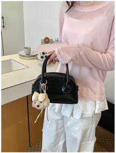 Detailed shot of a stylish black handbag with a cute puppy pendant, held by a model indoors.