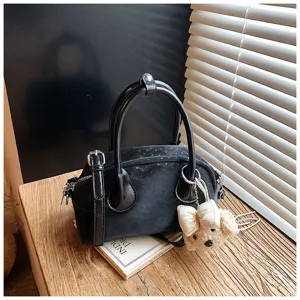 Detail shot of a stylish black women handbag with bow bear pendant and wood table background.