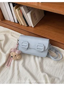 Detail shot of a chic light blue crossbody bag with double buckles and cute bear plush charm.