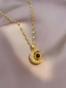 Detailed close up of gold crescent moon pendant necklace featuring sparkling chain and stones.