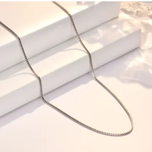 Close-up detail shot of a delicate s925 sterling silver box chain necklace, elegant shine.