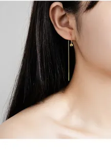 Nahaufnahme Detailaufnahme eines zarten vergoldeten Sterlingsilber Ohrfädels am Ohr.