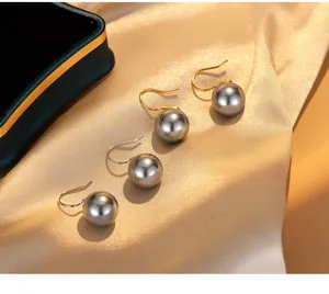 Detailansicht eleganter grauer Perlenohrringe mit Haken auf goldenem Seidenstoff.