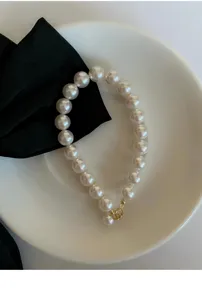 Detailaufnahme eines eleganten weißen Perlenarmbands mit goldenem Verschluss und Perle.