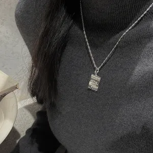 Close-up detail of a minimalist silver crumpled paper pendant necklace worn on a dark sweater.