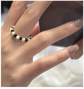 Gros plan détaillé d'une bague élastique perlée noire et blanche vintage sur une main.