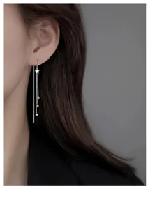 Gros plan détaillé de boucles d'oreilles longues étoile argentée avec chaînes et perles.