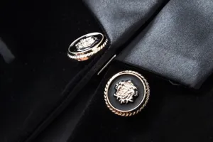 Detailed close-up of women's black velvet blazer featuring elegant metallic crest buttons and satin lapels.