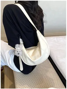 Dettaglio di una borsa a spalla bianca minimalista con un grazioso ciondolo in peluche.