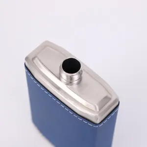 Detailed close-up of stainless steel hip flask with blue leather wrap and neat white stitching.