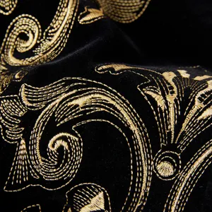 Close-up detail of luxurious black velvet fabric featuring intricate metallic gold baroque embroidery.