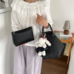 Vue détaillée du sac cabas en cuir tressé noir et de sa pochette avec charmant pendentif lapin.