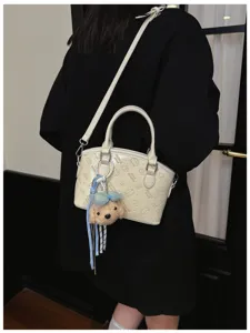 Detail view of white crossbody bag featuring embossed cartoon cat patterns and plush bear charm.