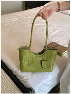 Detailed view of green woven leather tote bag handle and texture in bedroom lifestyle setting.