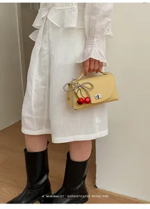 Detailed shot of yellow shoulder bag with beaded bow and cherry charm in daily outfit style