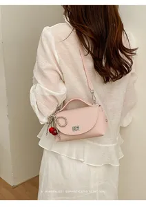 Chic pink shoulder cross-body bag with cute cherry charm and metallic twist-lock closure detail.