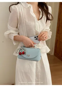 Close-up detail of a chic light blue shoulder bag featuring cute cherry charms and chain.