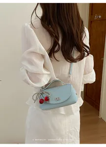 Detailed view of stylish light blue leather shoulder bag with chic cherry charm and turn lock.