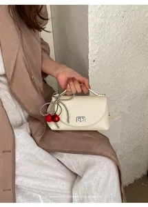 Detail shot of the white chic shoulder bag featuring a cute cherry charm and metallic clasp.