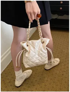 Detail view of cream quilted bucket bag with chain strap and drawstring closure.
