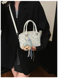Detail view of white PU leather crossbody bag featuring blue cartoon prints and plush puppy charm.