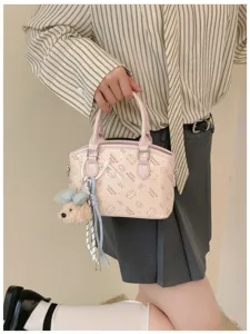 Pink cute mini handbag close-up, featuring cartoon print pattern and fluffy bear pendant.