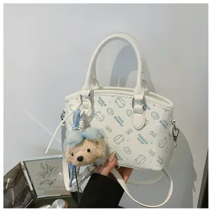 Detailed view of white cute crossbody bag with blue cartoon prints and plush bear pendant.