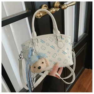 Detail view of white handbag with cute puppy plush pendant, blue cartoon print and shoulder strap.