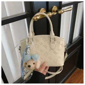 Cream handbag detail showcasing embossed cartoon cat patterns and cute plush pendant charm.
