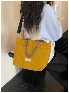 Detail shot of a casual yellow canvas tote bag with rope handles and black shoulder strap.