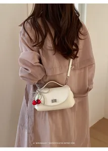 Detailed shot of retro white shoulder bag with cherry pendant and metal lock clasp.