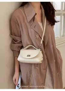Detailed shot of a chic white leather shoulder bag with top handle and metal lock accent.