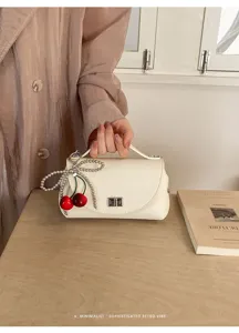 Detailed shot of a chic white mini handbag featuring a charming pearl bow and red cherry pendant.