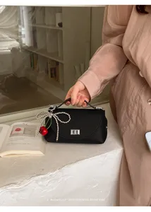 Black textured mini handbag featuring a silver twist lock, pearl bow and cherry charm.