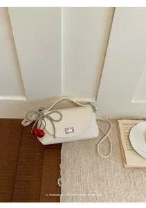 Detail shot of stylish white shoulder bag featuring a beaded bow and red cherry charm.