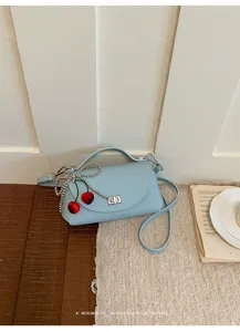 Exquisite detail of light blue leather crossbody bag with cute cherry charm and chain accent.