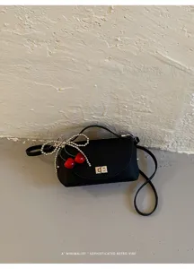 Minimalist black crossbody bag with beaded cherry bow charm, chic retro shoulder purse.