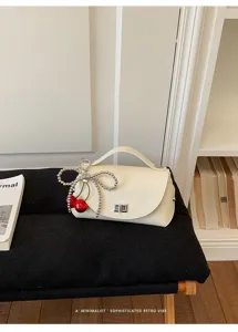 Close-up view of the chic off-white shoulder bag featuring a pearl bow and cherry charm.