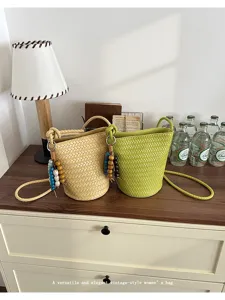 Detailed view of woven bucket bag with bead charm on wooden table lifestyle background.