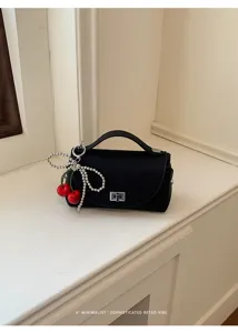 Black minimalist shoulder bag with chic pearl cherry charm and sleek metallic lock.