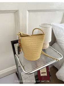 Stylish woven bucket bag with vintage charm, featuring braided handle and chic bead charm.
